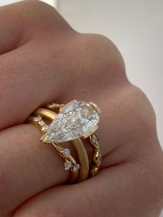 a woman's hand holding a gold ring with a pear shaped diamond