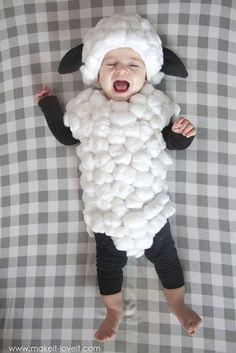 a baby wearing a sheep costume on top of a bed next to a checkered blanket