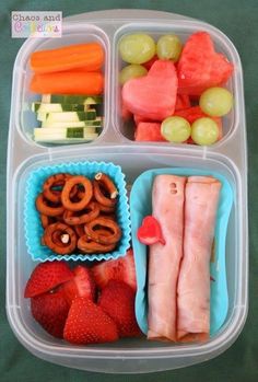 a plastic container filled with lots of food on top of a green table covered in fruit and veggies