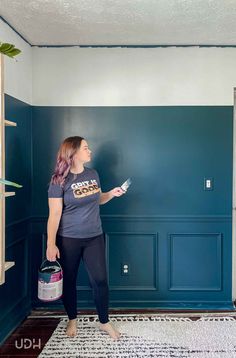 a woman standing in front of a blue wall holding a paint roller and painting the walls