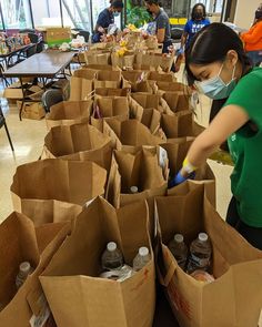 a woman wearing a face mask and gloves is cleaning up some brown bags with drinks