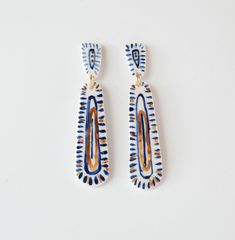 two pairs of blue and orange earrings on a white surface, one is shaped like a rectangle