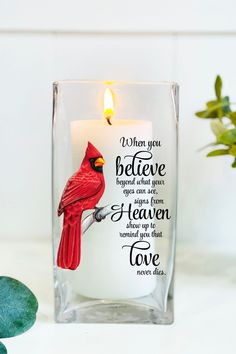 a glass candle holder with a cardinal on it and the words, when you believe