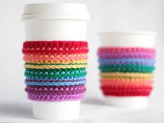 two coffee cups sitting next to each other in front of a white cup with colorful crochet on it