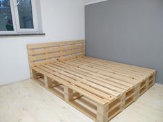 a bed made out of wooden pallets in a room with white walls and wood flooring