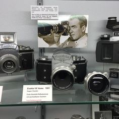 an assortment of old cameras on display in a glass case with pictures and other items