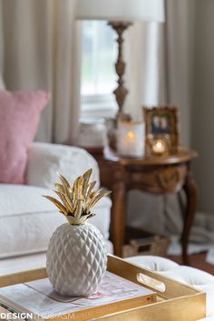 a white and gold tray with a pineapple on it in front of a couch