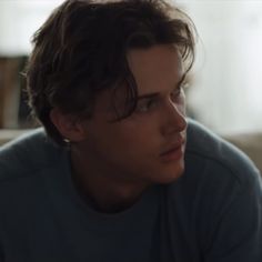 a young man sitting on top of a couch in front of a window looking off to the side