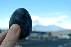 a hand holding an object in front of the camera, with mountains in the background