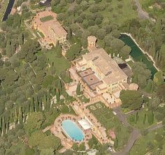 an aerial view of a large mansion with a pool in the center and trees surrounding it