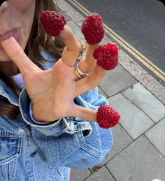 a woman with four raspberries on her fingers and two fingers in the air