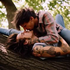 a man and woman laying on top of a tree in the forest kissing each other