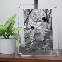 a black and white photo of a mother and child holding hands on a table next to a potted plant