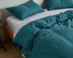 a bed with green sheets and pillows on top of it in a small room next to a wooden table