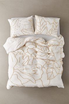 an unmade bed with white linen and gold leaf print on the comforter, along with two pillows