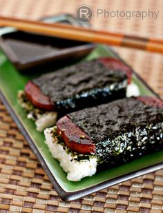 two pieces of sushi on a green plate with chopsticks