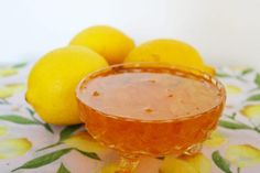 a glass bowl filled with liquid next to lemons on a floral table cloth,