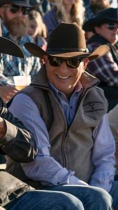 a group of men sitting next to each other in front of people wearing cowboy hats