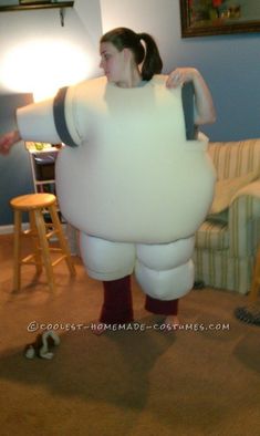 a woman standing in a living room with a giant white cloud costume over her shoulder