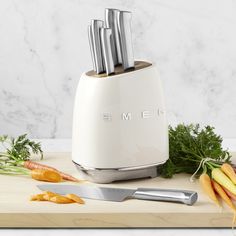 an electric knife holder with knives and carrots on a cutting board next to it