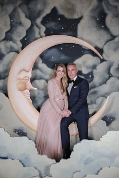 a man and woman posing for a photo in front of a painting of the moon