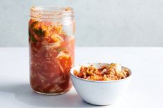 a jar filled with food next to a bowl full of pasta and sauce on a table