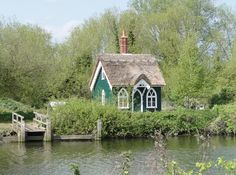 a small house with a thatched roof next to a body of water and trees