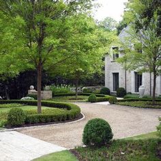 a garden with hedges and trees in front of a house