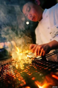 a chef is cooking on the grill with flames coming out of his hands and holding tongs