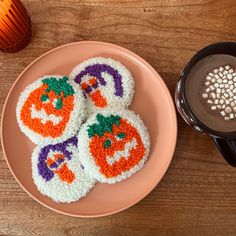 four crocheted pumpkin cookies on a plate next to a cup of hot chocolate