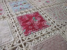 a crocheted blanket with pink and white squares on it, sitting on top of a bed