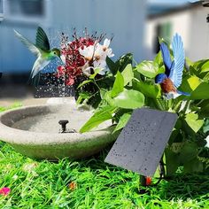 a bird bath sitting in the grass next to a flower pot with birds flying around it