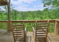 two rocking chairs sitting on a wooden deck overlooking the trees and mountains in the distance