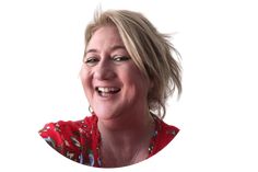 a woman with blonde hair smiling and wearing a red floral shirt, looking at the camera