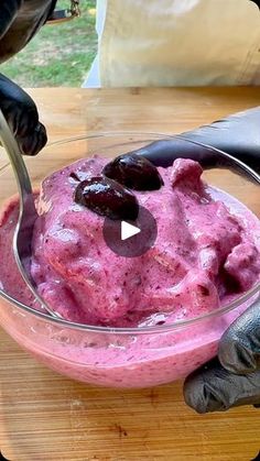 a bowl filled with pink ice cream on top of a wooden table next to a pair of gloves