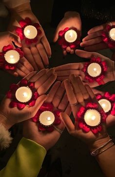 several people holding candles in their hands with red flowers on the palms and white ones around them