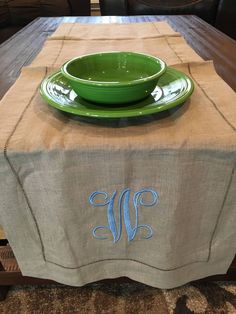 a green bowl sitting on top of a table with a monogrammed place mat