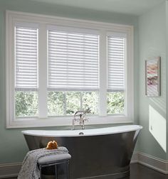 a bath tub sitting next to a window with blinds on the windowsill and a stool in front of it