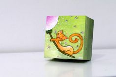 a small wooden block with a painting of a cat sitting on a tree branch in the background