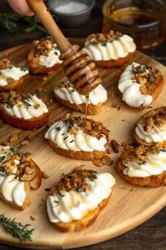 a wooden plate topped with mini cakes covered in whipped cream and walnuts next to a honey comb