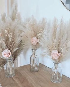 three glass vases with flowers in them sitting on a wooden table next to a mirror