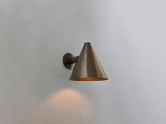 a wall light with a cone shaped shade on it's side against a white wall