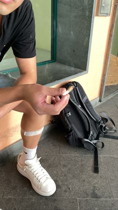 a man sitting on the ground next to a black bag and holding his cell phone