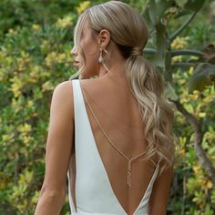 the back of a woman's white dress in front of some trees and bushes