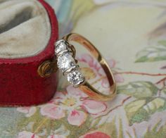 an engagement ring sitting on top of a red velvet box next to a flowered cloth