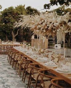 a long table is set with white plates and place settings for an outdoor dinner party