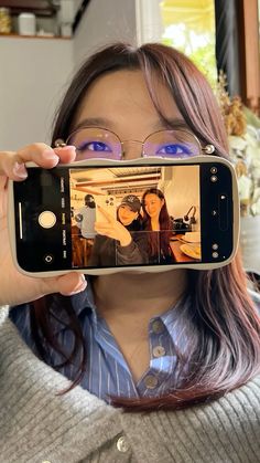 a woman holding up a cell phone to take a selfie with her reflection in it