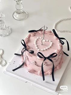 a pink cake with pearls and a heart shaped candle in the middle on a white table