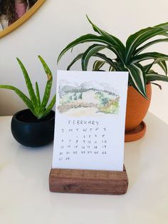 a calendar sitting on top of a wooden stand next to a potted aloei