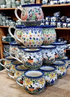 a stack of ceramic cups sitting on top of a wooden table next to shelves filled with dishes